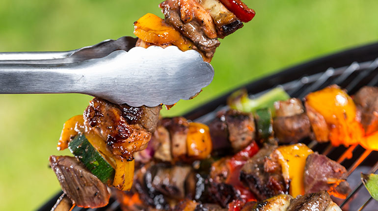 Pinzas sosteniendo una brocheta de carne